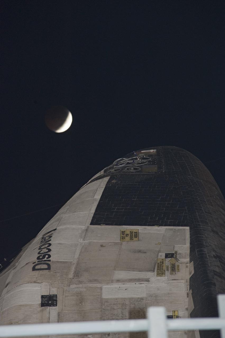 CAPE CANAVERAL, Fla. -- The beginning of a total lunar eclipse hovers over the top of space shuttle Discovery as the spacecraft waits to roll back from Launch Pad 39A to the Vehicle Assembly Building (VAB) at NASA's Kennedy Space Center in Florida. The move was scheduled for 12:30 a.m., but was postponed until 10 p.m. so technicians could resolve an issue with a leveling system on the crawler-transporter. Once inside the VAB, Discovery's external fuel tank will be examined and foam reapplied where 89 sensors were installed on the tank's aluminum skin for an instrumented tanking test on Dec. 17. The sensors were used to measure changes in the tank as super-cold propellants were pumped in and drained out. Data and analysis from the test will be used to determine what caused the tops of two, 21-foot-long support beams, called stringers, on the outside of the intertank to crack during fueling on Nov. 5.        Discovery's next launch opportunity is no earlier than Feb. 3, 2011. For more information on STS-133, visit www.nasa.gov/mission_pages/shuttle/shuttlemissions/sts133/. Photo credit: NASA/Kim Shiflett