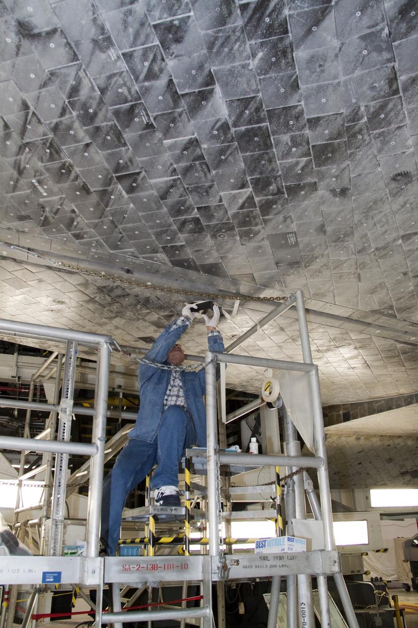 CAPE CANAVERAL, Fla. -- In Orbiter Processing Facility-1 at NASA's Kennedy Space Center in Florida, a thermal protection system technician is replacing a heat shield tile under space shuttle Atlantis. The tiles are part of the Orbiter Thermal Protection System, thermal shields to protect against temperatures as high as 3,000 degrees Fahrenheit, which are produced during descent for landing.  Atlantis is being prepared for the STS-135 mission, which will deliver the Raffaello multi-purpose logistics module packed with supplies, logistics and spare parts to the International Space Station. STS-135 is targeted to launch June 28, and will be the last spaceflight for the Space Shuttle Program. Photo credit: NASA/Jack Pfaller