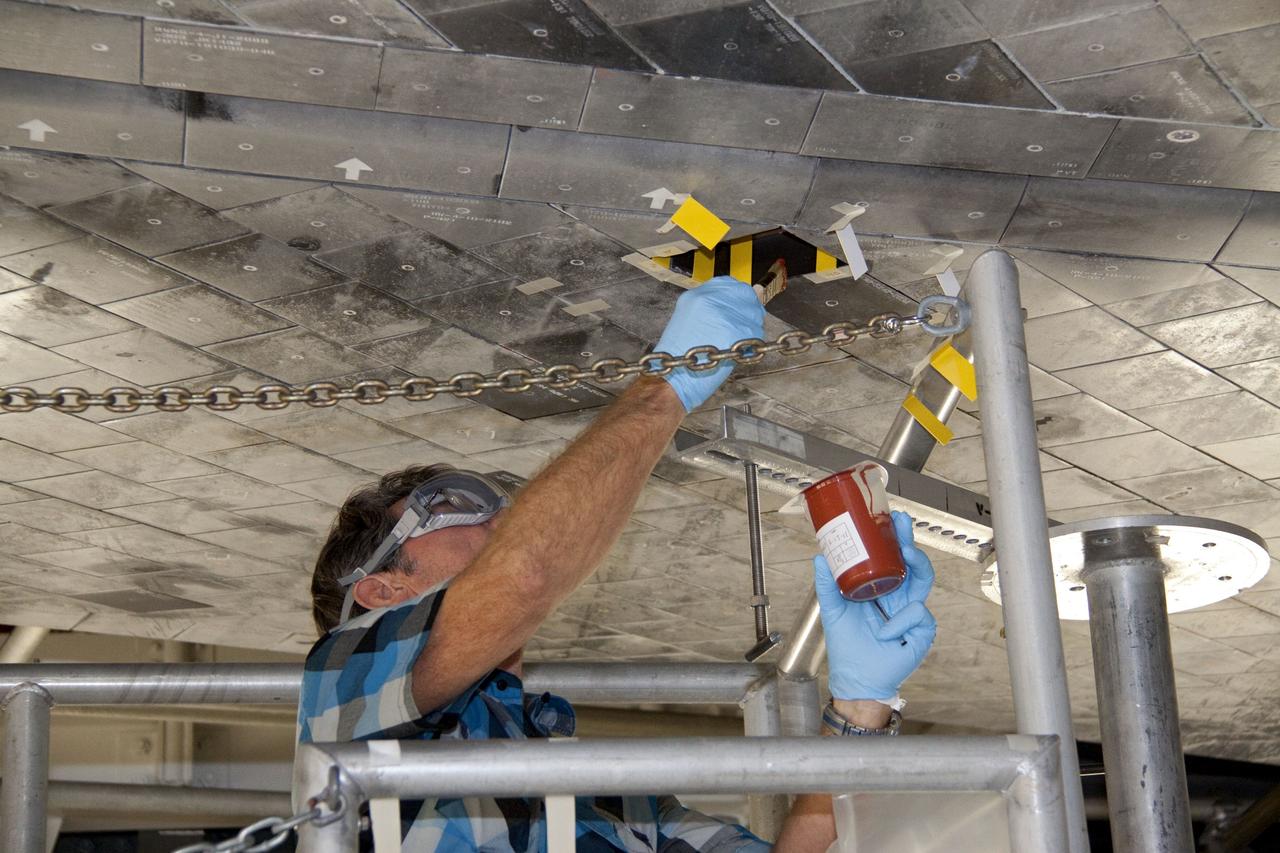 CAPE CANAVERAL, Fla. -- In Orbiter Processing Facility-1 at NASA's Kennedy Space Center in Florida, a thermal protection system technician applies a bonding agent to an area on space shuttle Atlantis' underside where a heat shield tile will be installed.         The tiles are part of the Orbiter Thermal Protection System that protects the shuttle against temperatures as high as 3,000 degrees Fahrenheit, which are produced during descent for landing. Atlantis is being prepared for the STS-135 mission, which will carry the Raffaello multi-purpose logistics module packed with supplies, logistics and spare parts to the International Space Station. STS-135 is targeted to launch June 28, and will be the last flight for the Space Shuttle Program. Photo credit: NASA/Jack Pfaller