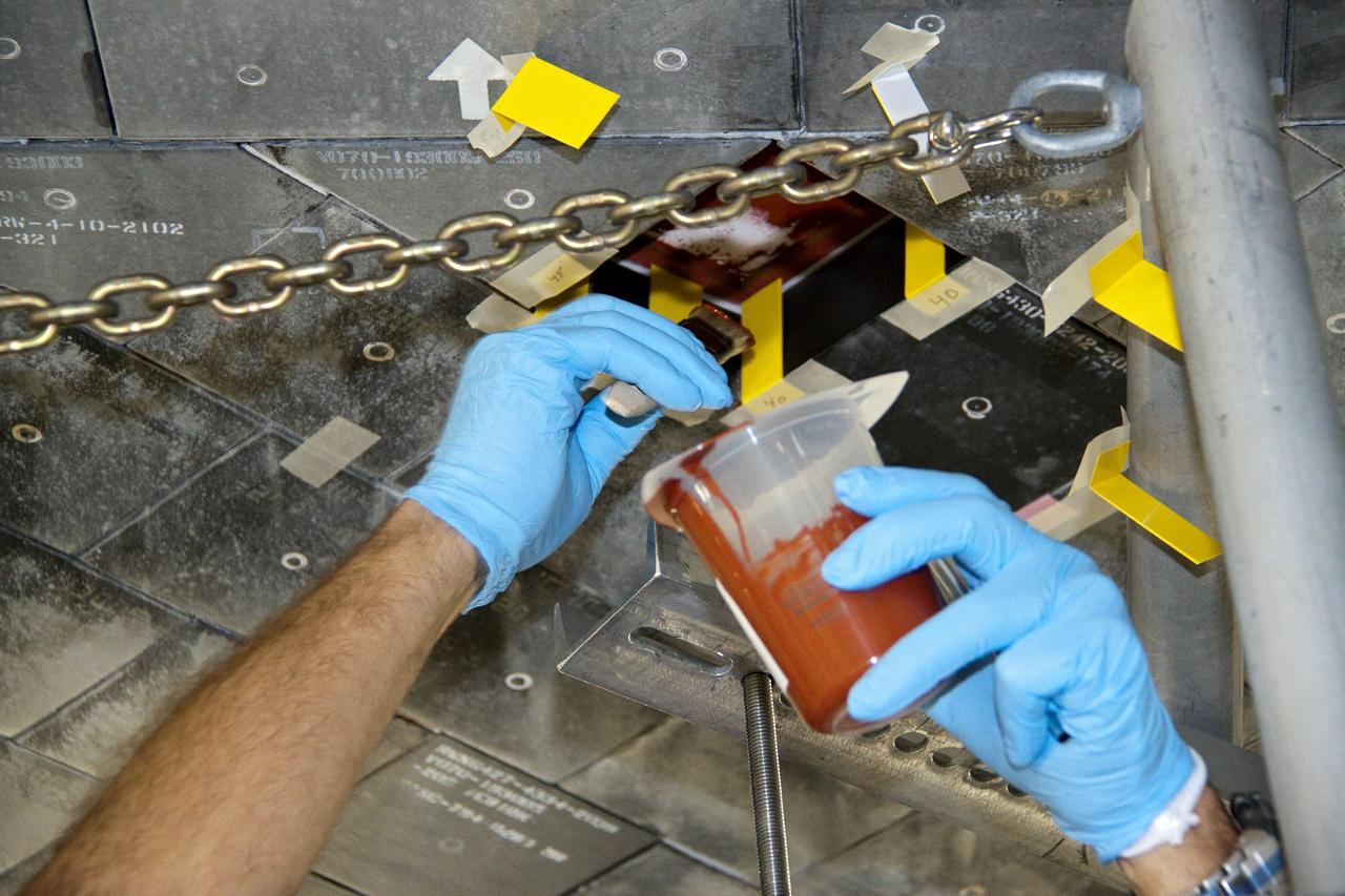 CAPE CANAVERAL, Fla. -- In Orbiter Processing Facility-1 at NASA's Kennedy Space Center in Florida, a thermal protection system technician applies a bonding agent to an area on space shuttle Atlantis' underside where a heat shield tile will be installed.         The tiles are part of the Orbiter Thermal Protection System that protects the shuttle against temperatures as high as 3,000 degrees Fahrenheit, which are produced during descent for landing. Atlantis is being prepared for the STS-135 mission, which will carry the Raffaello multi-purpose logistics module packed with supplies, logistics and spare parts to the International Space Station. STS-135 is targeted to launch June 28, and will be the last flight for the Space Shuttle Program. Photo credit: NASA/Jack Pfaller