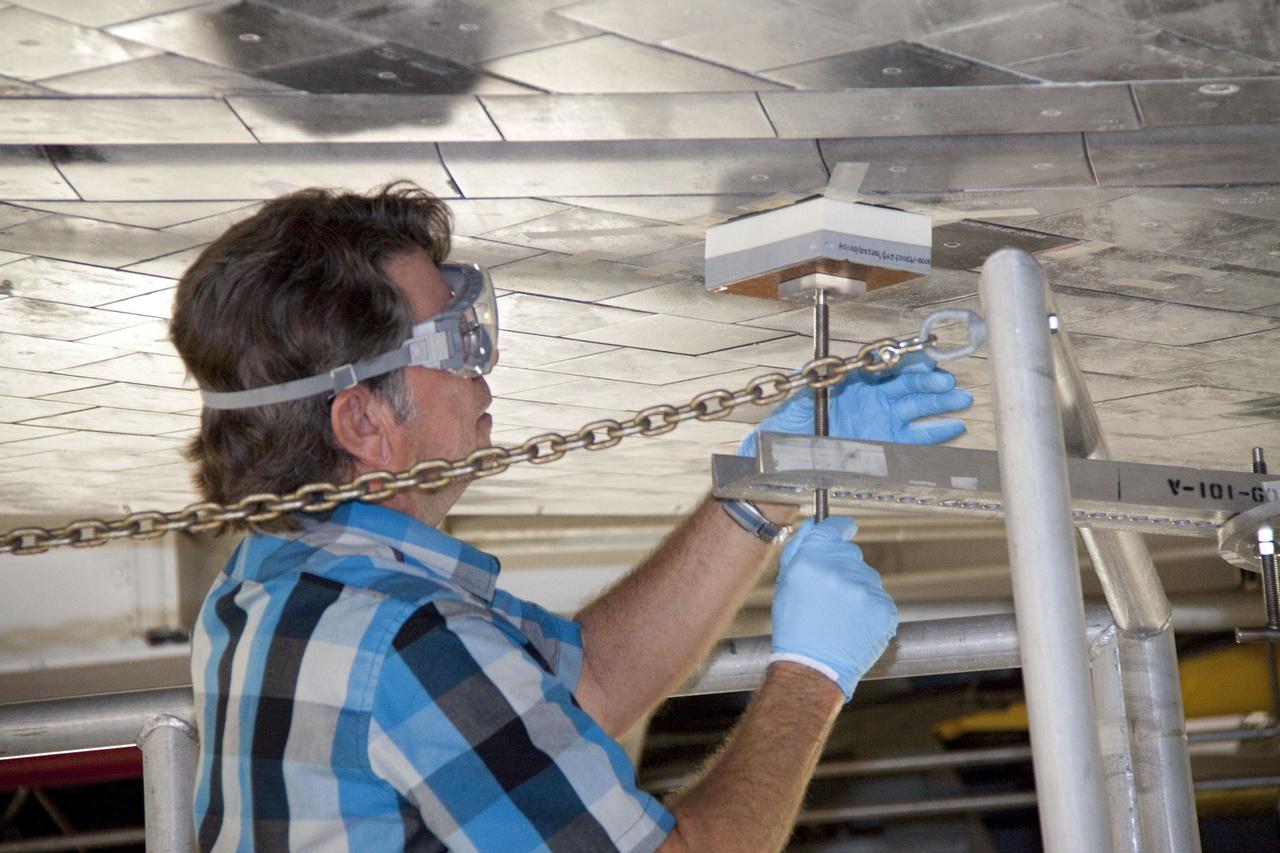 CAPE CANAVERAL, Fla. -- In Orbiter Processing Facility-1 at NASA's Kennedy Space Center in Florida, a thermal protection system technician secures a newly installed heat shield tile in place under space shuttle Atlantis with a pressure fitting to ensure a tight bond.      The tiles are part of the Orbiter Thermal Protection System that protects the shuttle against temperatures as high as 3,000 degrees Fahrenheit, which are produced during descent for landing. Atlantis is being prepared for the STS-135 mission, which will carry the Raffaello multi-purpose logistics module packed with supplies, logistics and spare parts to the International Space Station. STS-135 is targeted to launch June 28, and will be the last flight for the Space Shuttle Program. Photo credit: NASA/Jack Pfaller