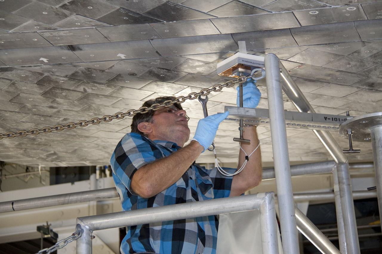 CAPE CANAVERAL, Fla. -- In Orbiter Processing Facility-1 at NASA's Kennedy Space Center in Florida, a thermal protection system technician secures a newly installed heat shield tile in place under space shuttle Atlantis with a pressure fitting to ensure a tight bond.    The tiles are part of the Orbiter Thermal Protection System that protects the shuttle against temperatures as high as 3,000 degrees Fahrenheit, which are produced during descent for landing. Atlantis is being prepared for the STS-135 mission, which will carry the Raffaello multi-purpose logistics module packed with supplies, logistics and spare parts to the International Space Station. STS-135 is targeted to launch June 28, and will be the last flight for the Space Shuttle Program. Photo credit: NASA/Jack Pfaller