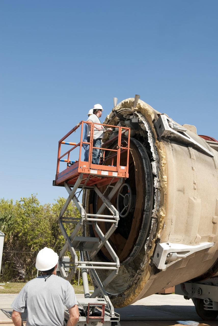 CAPE CANAVERAL, Fla. -- Workers at the Solid Rocket Booster Disassembly Facility at Hangar AF on Cape Canaveral Air Force Station in Florida, inspect the left spent booster used during space shuttle Discovery's final launch, after it was lowered onto a tracked dolly for processing.    The shuttle's two solid rocket booster casings and associated flight hardware are recovered in the Atlantic Ocean after every launch by Freedom Star and Liberty Star. The boosters impact the Atlantic about seven minutes after liftoff and the retrieval ships are stationed about 10 miles from the impact area at the time of splashdown. After the spent segments are processed, they will be transported to Utah, where they will be refurbished and stored, if needed. Photo credit: NASA/Jim Grossmann