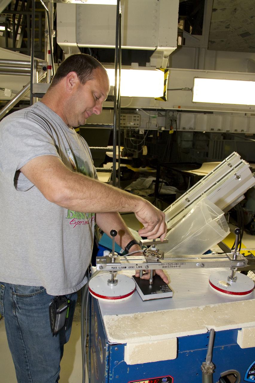CAPE CANAVERAL, Fla. -- A United Space Alliance technician examines one of shuttle Atlantis' thermal protection tiles in Orbiter Processing Facility-1 at NASA's Kennedy Space Center in Florida. The tile went through a pull test, which measured the force it took to pull it off of the shuttle in order to make sure the bond between the two is strong enough to withstand the force of launch and landing. Atlantis is being prepared for the STS-135 mission, which will deliver the Raffaello multipurpose logistics module packed with supplies, logistics and spare parts to the International Space Station. STS-135 is targeted to launch June 28, and will be the last spaceflight for the Space Shuttle Program. Photo credit: NASA/Jack Pfaller