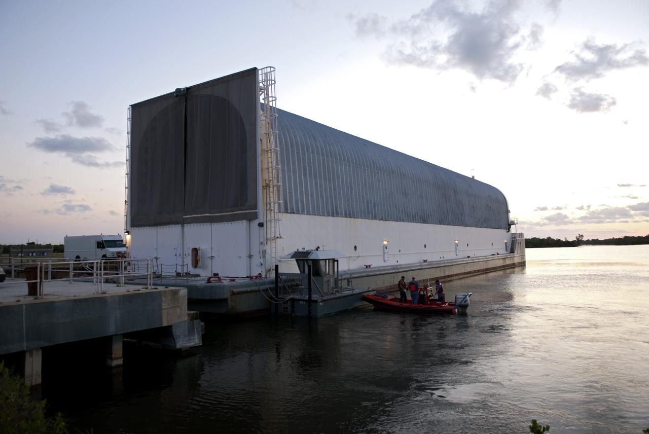 CAPE CANAVERAL, Fla. -- Workers in a skiff prepare the Pegasus Barge floating in the Launch Complex 39 area Turn Basin at NASA's Kennedy Space Center in Florida, for its move from the dock to a more secure mooring area. The barge is 266 ft long and 50 ft wide and has been used by the Space Shuttle Program to transport external fuel tanks over 900 miles of inland and open ocean waterways from the Michoud Assembly Facility in Louisiana to Kennedy. Photo credit: NASA/Jim Grossmann