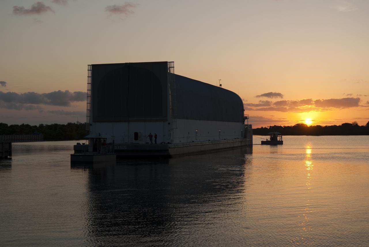 CAPE CANAVERAL, Fla. -- The morning sun rises over the Pegasus Barge floating in the Launch Complex 39 area Turn Basin at NASA's Kennedy Space Center in Florida, as it is being towed from the dock to a more secure mooring area. The barge is 266 ft long and 50 ft wide and has been used by the Space Shuttle Program to transport external fuel tanks over 900 miles of inland and open ocean waterways from the Michoud Assembly Facility in Louisiana to Kennedy. Photo credit: Jim Grossmann