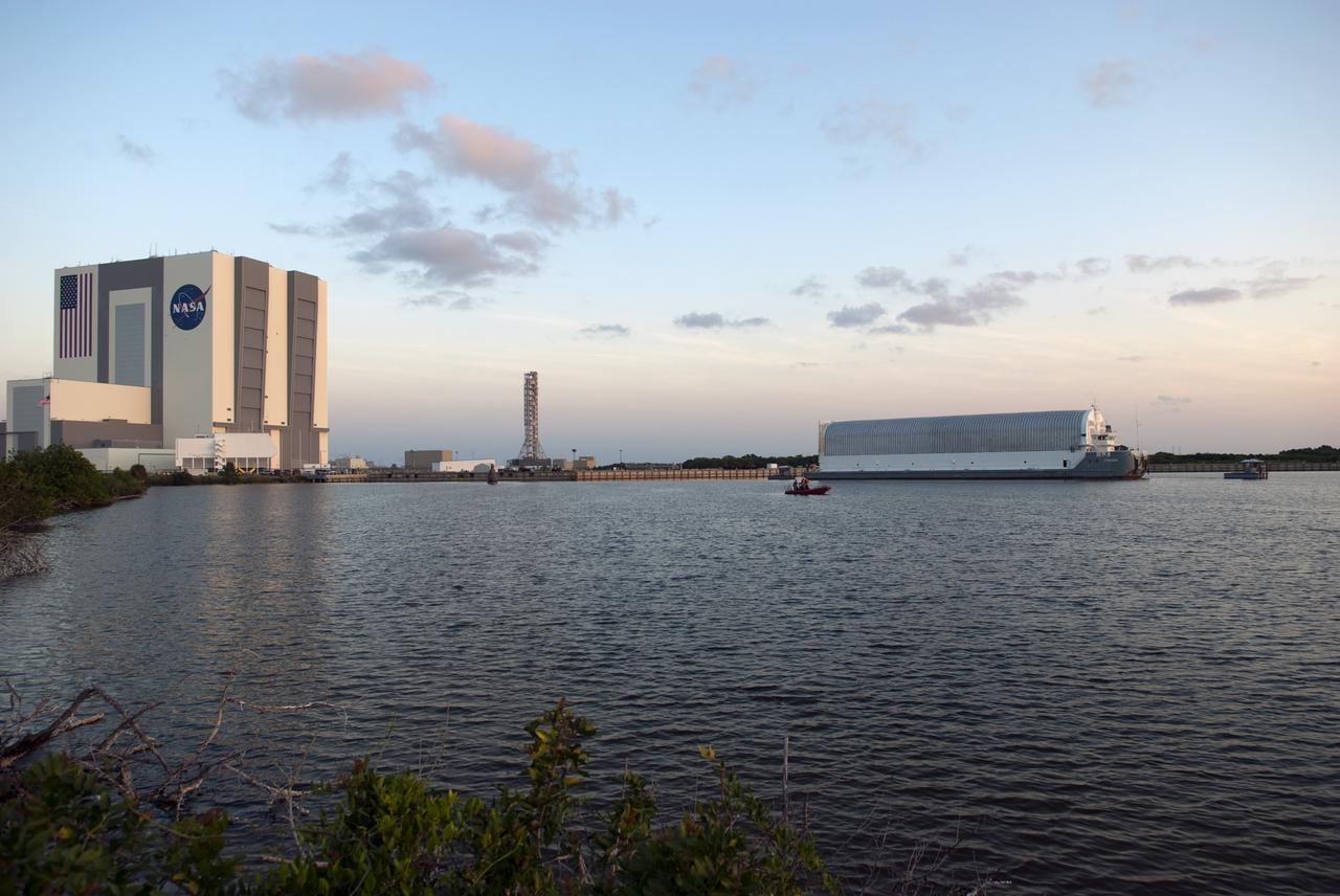 CAPE CANAVERAL, Fla. -- As the sun rises over the Vehicle Assembly Building at NASA's Kennedy Space Center in Florida, tugboats tow the Pegasus Barge from the dock in the Turn Basin to a more secure mooring area. The barge is 266 ft long and 50 ft wide and has been used by the Space Shuttle Program to transport external fuel tanks over 900 miles of inland and open ocean waterways from the Michoud Assembly Facility in Louisiana to Kennedy. Photo credit: NASA/Jim Grossmann