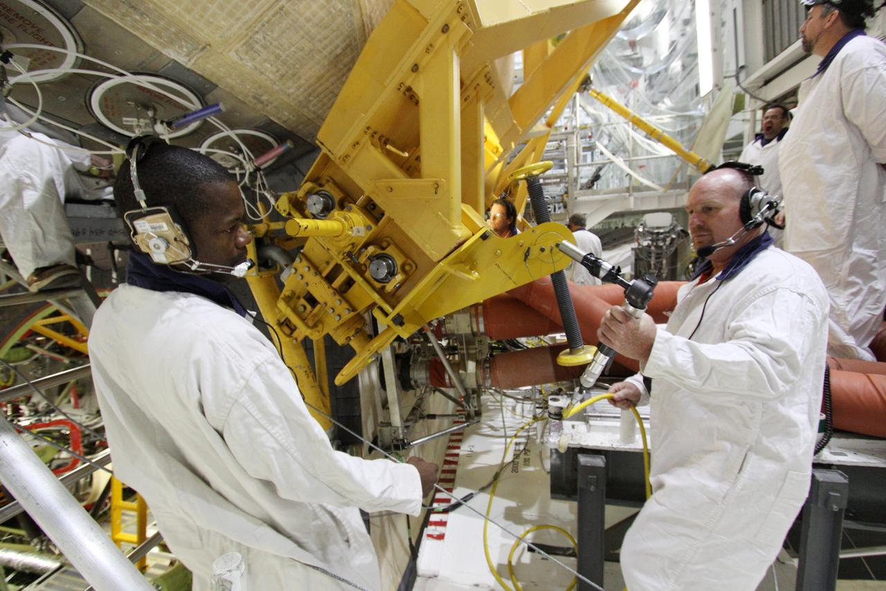 CAPE CANAVERAL, Fla. - In Orbiter Processing Facility-2 at NASA's Kennedy Space Center in Florida, workers use a crane to grapple shuttle Discovery's right-hand orbital maneuvering system, or OMS, pod for removal. It then will be transported to the Hypergol Maintenance Facility. The removal is part of Discovery's transition and retirement processing. Work performed on Discovery is expected to help rocket designers build next-generation spacecraft and prepare the shuttle for future public display. Photo credit: NASA/Troy Cryder
