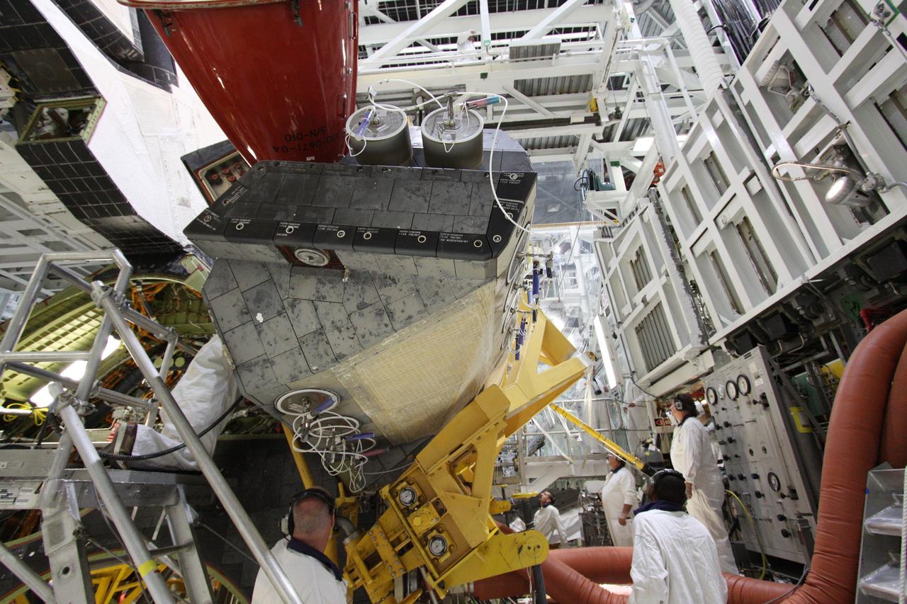 CAPE CANAVERAL, Fla. - In Orbiter Processing Facility-2 at NASA's Kennedy Space Center in Florida, workers use a crane to grapple shuttle Discovery's right-hand orbital maneuvering system, or OMS, pod for removal. It then will be transported to the Hypergol Maintenance Facility. The removal is part of Discovery's transition and retirement processing. Work performed on Discovery is expected to help rocket designers build next-generation spacecraft and prepare the shuttle for future public display. Photo credit: NASA/Troy Cryder