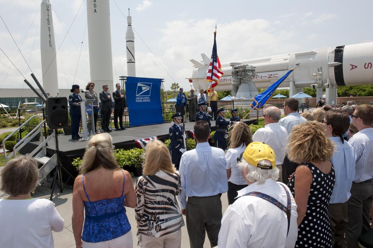 CAPE CANAVERAL, Fla. -- In the Rocket Garden at NASA's Kennedy Space Center Visitor Complex in Florida, the audience and speakers stand for the Pledge of Allegiance and the singing of the National Anthem by a member of the 45th Space Wing Honor Guard from Patrick Air Force Base in Florida. Also on stage are, from left, Director of Education and External Relations for Kennedy Cheryl Hurst, Center Director Bob Cabana and United States Postal Service official Steve Massey, Mercury Astronaut Scott Carpenter, NASA Administrator, Charlie Bolden, Julie Jenkins and NASA's Deputy Director for Planetary Science, Jim Adams, all in attendance for the United States Postal Service unveiling of two new stamps to commemorate the 50th anniversary of human spaceflight.              One stamp commemorates NASA's Project Mercury and Alan Shepard's historic launch on May 5, 1961, aboard the spacecraft Freedom 7. The second stamp honors NASA's MESSENGER, which reached Mercury in March to become the first spacecraft to orbit the planet. The two missions frame a remarkable 50-year period in which America advanced space exploration through more than 1,500 crewed and uncrewed flights. Photo credit: NASA/Kim Shiflett