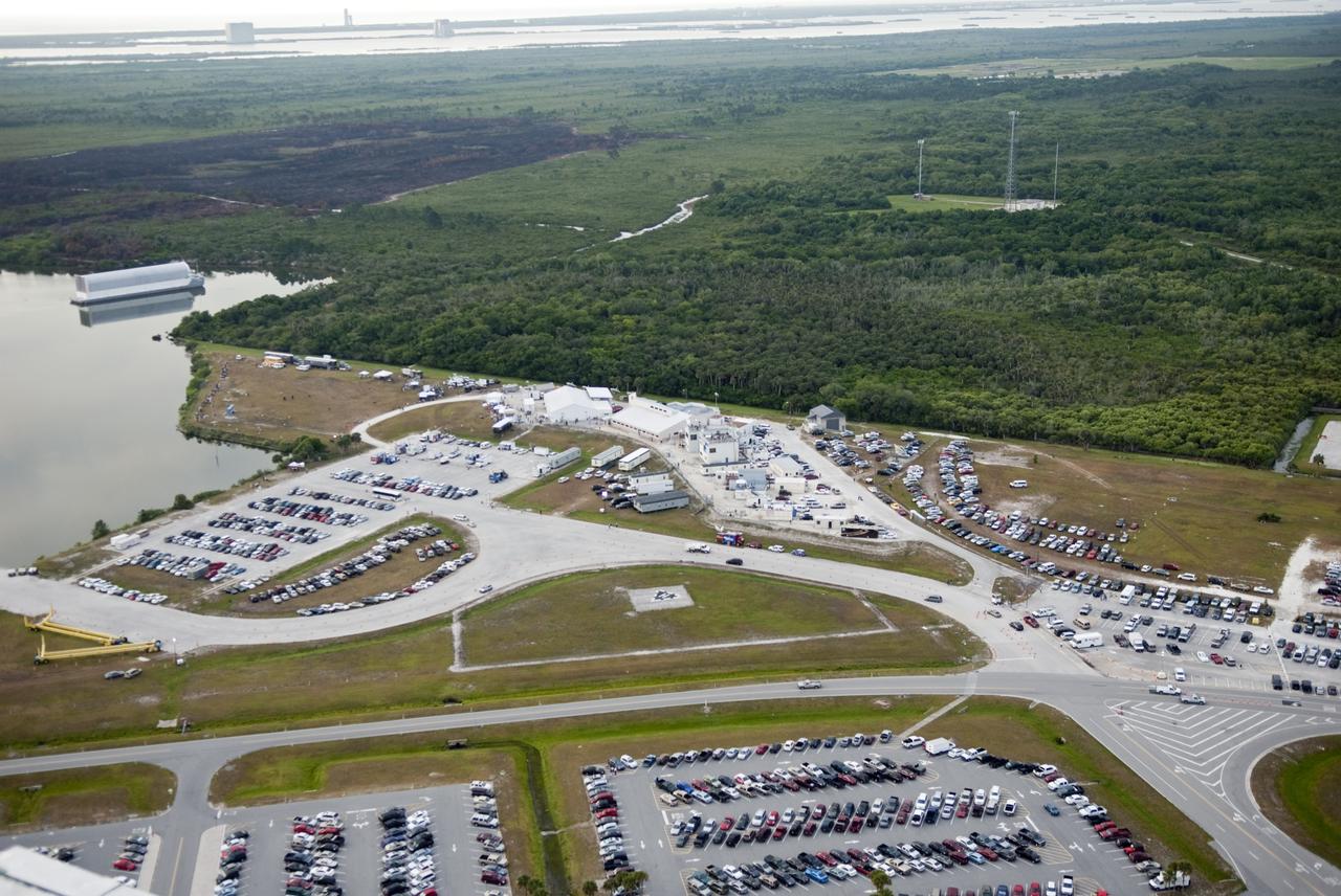 CAPE CANAVERAL, Fla. -- In this image taken from the Vehicle Assembly Building roof at NASA's Kennedy Space Center in Florida seen is the Press Site complex, the Turn Basin with the Pegasus Barge moored in an alcove, the myriad of vehicles, satellite trucks and trailers belonging to invited guests and media for the launch of space shuttle Endeavour. In the background the grassy-treed area is part of the Merritt Island Wildlife Refuge on the center, which stretches to the shore line that encompasses the launch pads.              Endeavour began its final flight, the STS-134 mission, to the International Space Station on time at 8:56 a.m. EDT on May 16. Endeavour and its six-member crew are embarking on a mission to deliver the Alpha Magnetic Spectrometer-2 (AMS), Express Logistics Carrier-3, a high-pressure gas tank and additional spare parts for the Dextre robotic helper to the space station. Endeavour's first launch attempt on April 29 was scrubbed because of an issue associated with a faulty power distribution box called the aft load control assembly-2 (ALCA-2). For more information visit, www.nasa.gov/mission_pages/shuttle/shuttlemissions/sts134/index.html. Kennedy coexists with the Merritt Island National Wildlife Refuge, habitat to more than 310 species of birds, 25 mammals, 117 fish and 65 amphibians and reptiles. Photo credit: NASA/Jim Grossmann