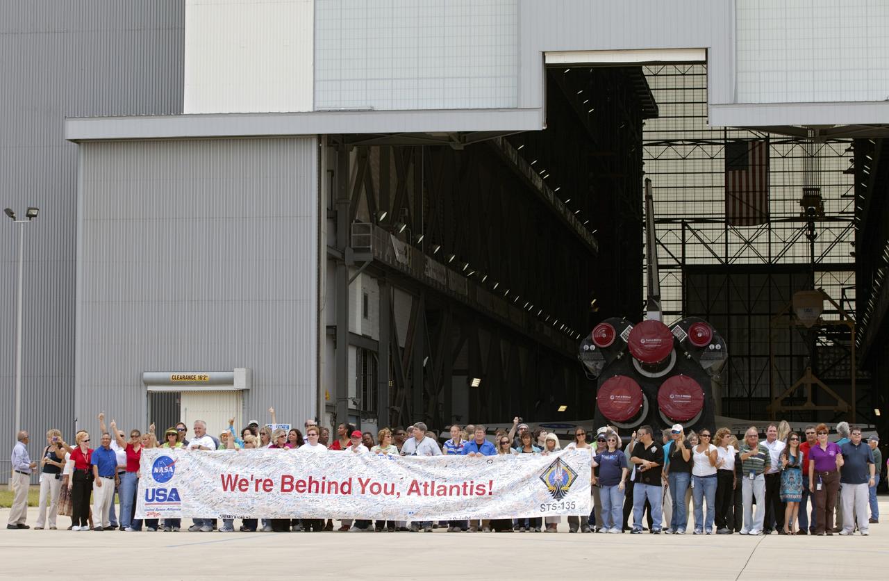 CAPE CANAVERAL, Fla. -- Kennedy employees hold up a "We're Behind You, Atlantis" banner after shuttle Atlantis' move, or rollover, to the Vehicle Assembly Building (VAB) at NASA's Kennedy Space Center in Florida.             The move called "rollover" is a major milestone in processing for the STS-135 mission to the International Space Station. Commander Chris Ferguson, Pilot Doug Hurley and Mission Specialists Sandra Magnus and Rex Walheim are targeted to launch in early July, taking with them the Raffaello multipurpose logistics module packed with supplies, logistics and spare parts. The STS-135 mission also will fly a system to investigate the potential for robotically refueling existing spacecraft and return a failed ammonia nfor future systems. STS-135 will be the 33rd flight of Atlantis, the 37th shuttle mission to the space station, and the 135th and final mission of NASA's Space Shuttle Program. For more information visit, www.nasa.gov/mission_pages/shuttle/shuttlemissions/sts135/index.html. Photo credit: NASA/Frankie Martin