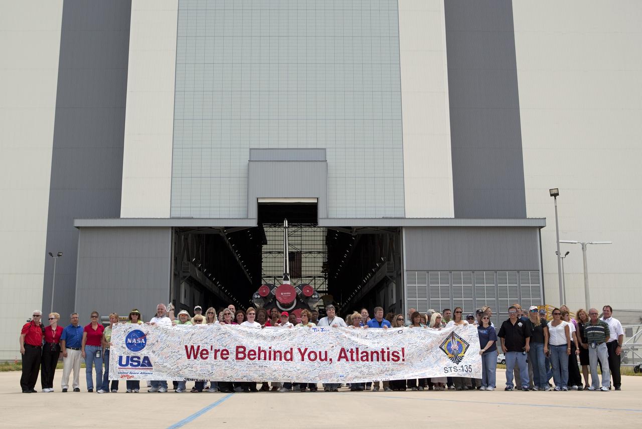 CAPE CANAVERAL, Fla. -- Kennedy employees hold up a "We're Behind You, Atlantis" banner after shuttle Atlantis' move, or rollover, to the Vehicle Assembly Building (VAB) at NASA's Kennedy Space Center in Florida.      The move called "rollover" is a major milestone in processing for the STS-135 mission to the International Space Station. Inside the VAB, the shuttle will be attached to its external fuel tank and solid rocket boosters. Commander Chris Ferguson, Pilot Doug Hurley and Mission Specialists Sandra Magnus and Rex Walheim are targeted to launch in early July, taking with them the Raffaello multipurpose logistics module packed with supplies, logistics and spare parts. The STS-135 mission also will fly a system to investigate the potential for robotically refueling existing spacecraft and return a failed ammonia pump module to help NASA better understand the failure mechanism and improve pump designs for future systems. STS-135 will be the 33rd flight of Atlantis, the 37th shuttle mission to the space station, and the 135th and final mission of NASA's Space Shuttle Program. For more information visit, www.nasa.gov/mission_pages/shuttle/shuttlemissions/sts135/index.html. Photo credit: NASA/Dimitri Gerondidakis