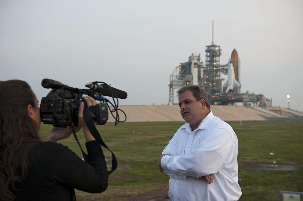 CAPE CANAVERAL, Fla. -- Near Launch Pad 39A at NASA's Kennedy Space Center in Florida, Payload Mission Manager Joe Delai speaks to media. The Raffaello multi-purpose logistics module (MPLM) was delivered to the pad overnight and lifted into the payload changeout room. The payload ground-handling mechanism then will be used to transfer Raffaello out of the canister into Atlantis' payload bay. Next, the rotating service structure that protects the shuttle from the elements and provides access will be rotated back into place. In the background is shuttle Atlantis, waiting to launch on the STS-135 mission.              Commander Chris Ferguson, Pilot Doug Hurley and Mission Specialists Sandra Magnus and Rex Walheim are targeted to lift off on space shuttle Atlantis July 8, taking with them the MPLM packed with supplies, logistics and spare parts to the International Space Station. The STS-135 mission also will fly a system to investigate the potential for robotically refueling existing satellites and return a failed ammonia pump module to help NASA better understand the failure mechanism and improve pump designs for future systems. STS-135 will be the 33rd flight of Atlantis, the 37th shuttle mission to the space station, and the 135th and final mission of NASA's Space Shuttle Program. For more information visit, www.nasa.gov/mission_pages/shuttle/shuttlemissions/sts135/index.html. Photo credit: NASA/Kim Shiflett