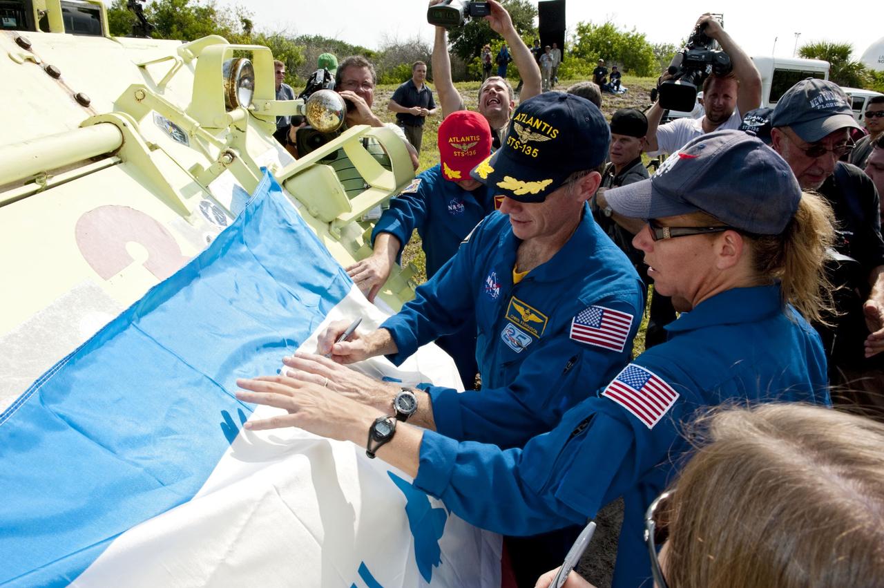 CAPE CANAVERAL, Fla. -- The STS-135 crew sign their names to an Atlantis flag at the conclusion of their M113 armored personnel carrier training at NASA's Kennedy Space Center in Florida. Seen here are Mission Specialist Sandy Magnus (right) and Commander Chris Ferguson. An M113 is kept at the foot of the launch pad in case an emergency exit from the launch pad is needed and every shuttle crew is trained on driving the vehicle before launch. The STS-135 crew is at Kennedy to participate in a launch countdown dress rehearsal called the Terminal Countdown Demonstration Test (TCDT) and related training.       Atlantis and its crew are targeted to lift off July 8, taking with them the Raffaello multi-purpose logistics module packed with supplies and spare parts to the International Space Station. The STS-135 mission also will fly a system to investigate the potential for robotically refueling existing satellites and return a failed ammonia pump module to help NASA better understand the failure mechanism and improve pump designs for future systems. STS-135 will be the 33rd flight of Atlantis, the 37th shuttle mission to the space station, and the 135th and final mission of NASA's Space Shuttle Program. For more information visit, www.nasa.gov/mission_pages/shuttle/shuttlemissions/sts135/index.html. Photo credit: NASA/Kim Shiflett