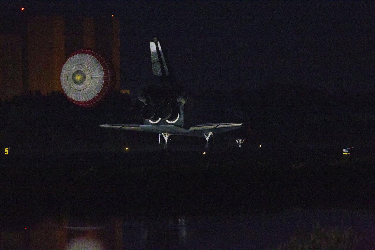 CAPE CANAVERAL, Fla. -- Space shuttle Atlantis, trailed by its drag chute, lands on Runway 15 at the Shuttle Landing Facility at NASA's Kennedy Space Center in Florida. In the background is the Vehicle Assembly Building, still engulfed in darkness.  Securing the space shuttle fleet's place in history, Atlantis marked the 26th nighttime landing of NASA's Space Shuttle Program and the 78th landing at Kennedy. Main gear touchdown was at 5:57:00 a.m. EDT, followed by nose gear touchdown at 5:57:20 a.m., and wheelstop at 5:57:54 a.m. On board are STS-135 Commander Chris Ferguson, Pilot Doug Hurley, and Mission Specialists Sandra Magnus and Rex Walheim.    On the 37th shuttle mission to the International Space Station, STS-135 delivered the Raffaello multi-purpose logistics module filled with more than 9,400 pounds of spare parts, equipment and supplies that will sustain station operations for the next year. STS-135 was the 33rd and final flight for Atlantis, which has spent 307 days in space, orbited Earth 4,848 times and traveled 125,935,769 miles. STS-135 also was the final mission of the Space Shuttle Program.  For more information, visit www.nasa.gov/mission_pages/shuttle/shuttlemissions/sts135/index.html. Photo credit: NASA/Kenny Allen