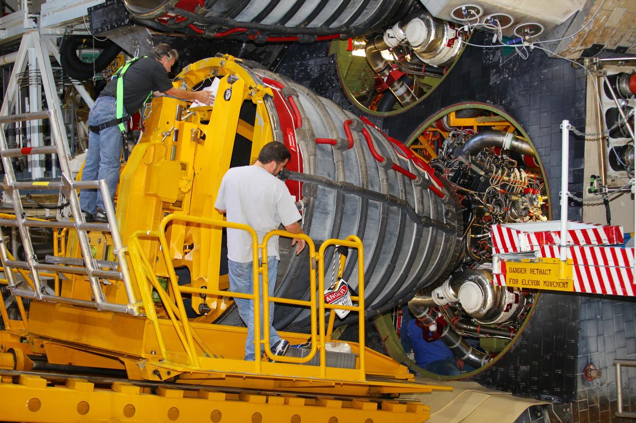 CAPE CANAVERAL, Fla. -- In Orbiter Processing Facility-2 at NASA’s Kennedy Space Center in Florida, technicians monitor the progress as they use a Hyster forklift to position an engine removal device on Engine #3 on space shuttle Atlantis. Inside the aft section, a technician disconnects hydraulic, fluid and electrical lines. The forklift will be used to remove the engine and transport it to the Engine Shop for possible future use. Each of the three space shuttle main engines is 14 feet long and weighs 7,800 pounds. Removal of the space shuttle main engines is part of the Transition and Retirement work that is being performed in order to prepare Atlantis for eventual display at the Kennedy Space Center Visitor Complex in Florida. Photo credit: Frankie Martin