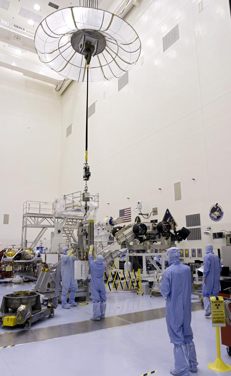CAPE CANAVERAL, Fla. -- In the high bay of the Payload Hazardous Servicing Facility (PHSF) at NASA's Kennedy Space Center in Florida, a crane lifts the multi-mission radioisotope thermoelectric generator (MMRTG) for NASA's Mars Science Laboratory (MSL) mission from its support base, at left, toward the MMRTG integration cart behind it. The cart will be used to install the MMRTG on the Curiosity rover for a fit check. The rover appears above the heads of the spacecraft technicians, at right. The MMRTG will be installed on the rover for launch at the pad.    The MMRTG will generate the power needed for the mission from the natural decay of plutonium-238, a non-weapons-grade form of the radioisotope. Heat given off by this natural decay will provide constant power through the day and night during all seasons. Curiosity, MSL's car-sized rover, has 10 science instruments designed to search for signs of life, including methane, and help determine if the gas is from a biological or geological source. Waste heat from the MMRTG will be circulated throughout the rover system to keep instruments, computers, mechanical devices and communications systems within their operating temperature ranges. Launch of MSL aboard a United Launch Alliance Atlas V rocket is planned for Nov. 25 from Space Launch Complex 41 on Cape Canaveral Air Force Station. For more information, visit http://www.nasa.gov/msl. Photo credit: NASA/Cory Huston