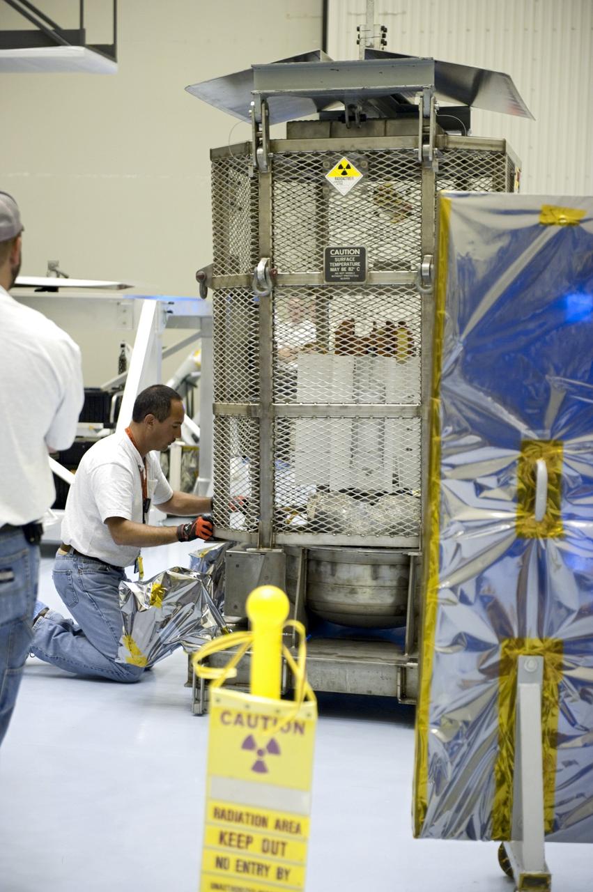 CAPE CANAVERAL, Fla. -- In the airlock of the Payload Hazardous Servicing Facility at NASA's Kennedy Space Center in Florida, a Department of Energy employee positions the mesh container, known as the "gorilla cage," on the support base of the multi-mission radioisotope thermoelectric generator (MMRTG) for NASA's Mars Science Laboratory (MSL) mission. The mobile plexiglass radiation shields, in the foreground at right, helps minimize the employees' radiation exposure. The cage protects the MMRTG during transport and allows any excess heat generated to dissipate into the air. Transport of the MMRTG to the RTG storage facility follows the completion of the MMRTG fit check on the Curiosity rover.     The MMRTG will generate the power needed for the mission from the natural decay of plutonium-238, a non-weapons-grade form of the radioisotope. Heat given off by this natural decay will provide constant power through the day and night during all seasons. MSL's components include a car-sized rover, Curiosity, which has 10 science instruments designed to search for signs of life, including methane, and help determine if the gas is from a biological or geological source. Waste heat from the MMRTG will be circulated throughout the rover system to keep instruments, computers, mechanical devices and communications systems within their operating temperature ranges. Launch of MSL aboard a United Launch Alliance Atlas V rocket is targeted for Nov. 25 from Space Launch Complex 41 on Cape Canaveral Air Force Station. For more information, visit http://www.nasa.gov/msl. Photo credit: NASA/Kim Shiflett