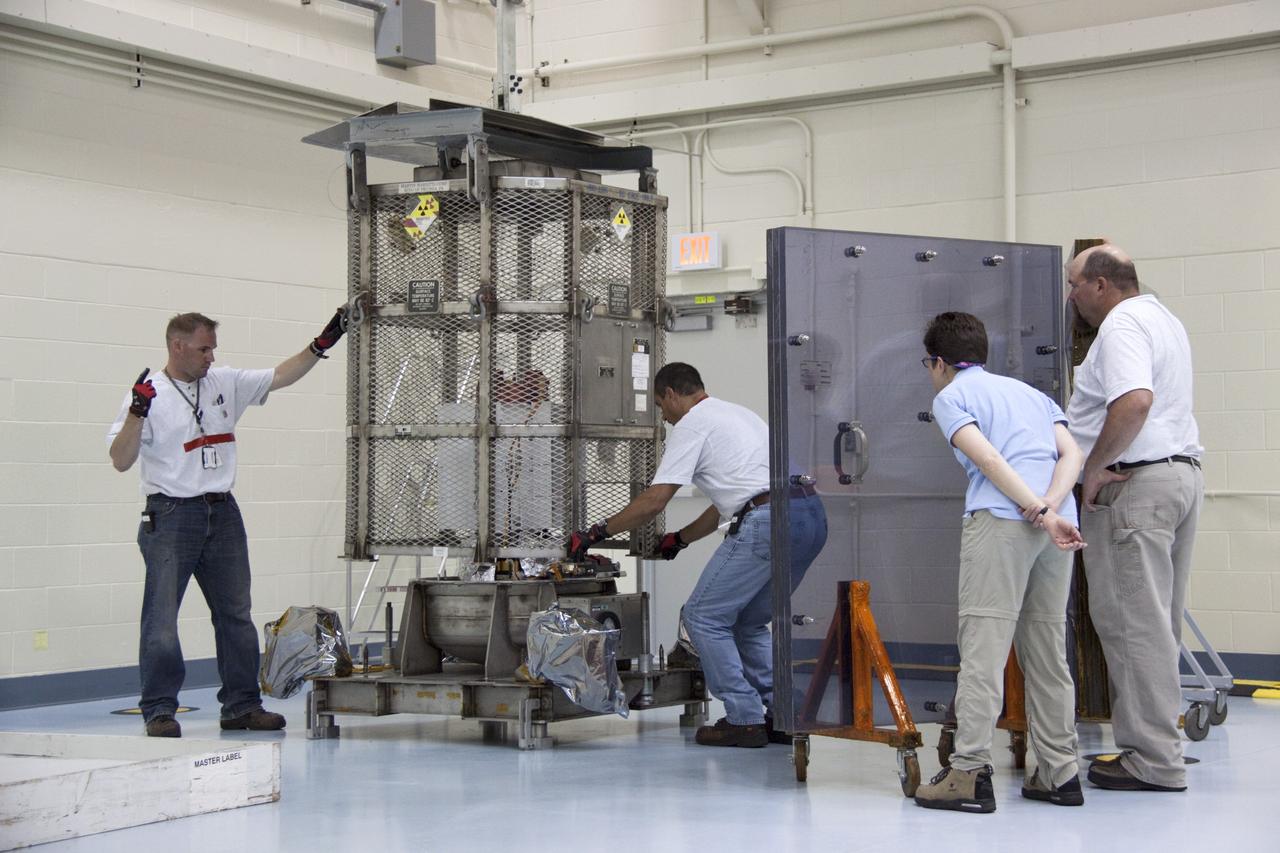 CAPE CANAVERAL, Fla. -- In the high bay of the RTG storage facility (RTGF) at NASA's Kennedy Space Center in Florida, Department of Energy workers guide the mesh container enclosing the multi-mission radioisotope thermoelectric generator (MMRTG) for NASA's Mars Science Laboratory (MSL) mission as it is lifted by a crane. The container, known as the "gorilla cage," protects the MMRTG during transport and allows any excess heat generated to dissipate into the air.  The cage is being removed from around the MMRTG following it return to the RTGF from a fit check on MSL's Curiosity rover in the Payload Hazardous Servicing Facility (PHSF).  The workers at right are observing the operation from behind a mobile plexiglass radiation shield to minimize their radiation exposure.    The MMRTG will generate the power needed for the mission from the natural decay of plutonium-238, a non-weapons-grade form of the radioisotope. Heat given off by this natural decay will provide constant power through the day and night during all seasons. MSL's components include a compact car-sized rover, Curiosity, which has 10 science instruments designed to search for signs of life, including methane, and help determine if the gas is from a biological or geological source. Waste heat from the MMRTG will be circulated throughout the rover system to keep instruments, computers, mechanical devices and communications systems within their operating temperature ranges. Launch of MSL aboard a United Launch Alliance Atlas V rocket is targeted for Nov. 25 from Space Launch Complex 41 on Cape Canaveral Air Force Station. For more information, visit http://www.nasa.gov/msl. Photo credit: NASA/Troy Cryder