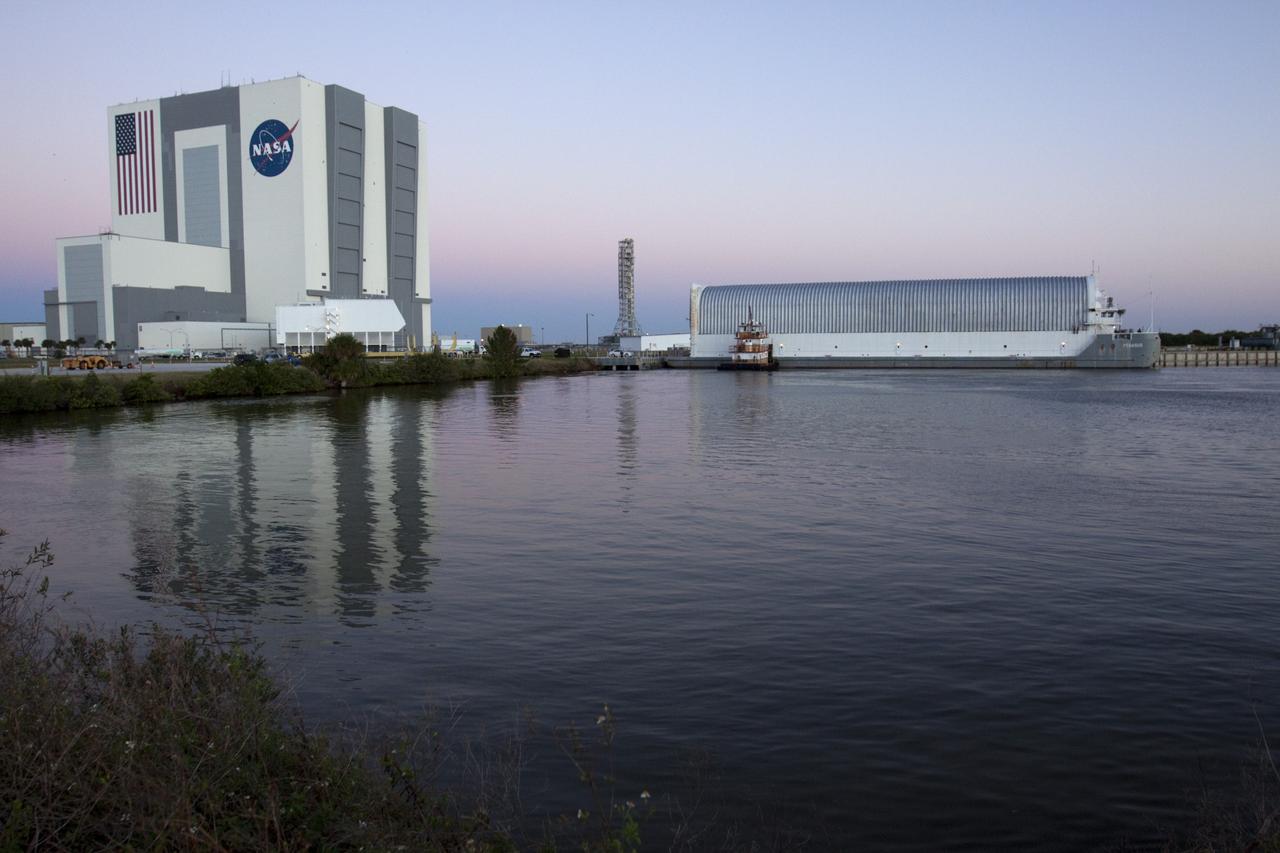 CAPE CANAVERAL, Fla. – In the Turn Basin in the Launch Complex 39 area at NASA's Kennedy Space Center in Florida, the Vehicle Assembly Building and Mobile Launcher are reflected in the water beside where a tugboat and the Pegasus Barge are moored. The 266-foot-long and 50-foot-wide barge will be towed by NASA's Freedom Star ship to deliver space shuttle main engine (SSME) ground support equipment to Stennis Space Center near Bay St. Louis, Miss. Since being delivered to NASA in 1999, Pegasus sailed 41 times and transported 31 shuttle external fuel tanks from Michoud Assembly Facility near New Orleans to Kennedy. The barge will leave Kennedy, perhaps for the final time. Both the barge and shuttle equipment will remain in storage until their specific future uses are determined. The SSMEs themselves will be transported to Stennis separately for use with the agency’s new heavy-lift rocket, the Space Launch System. The work is part of the Space Shuttle Program’s transition and retirement processing. For more information about Shuttle Transition and Retirement, visit http://www.nasa.gov/mission_pages/transition/home/index.html. Photo credit: NASA/ Kim Shiflett