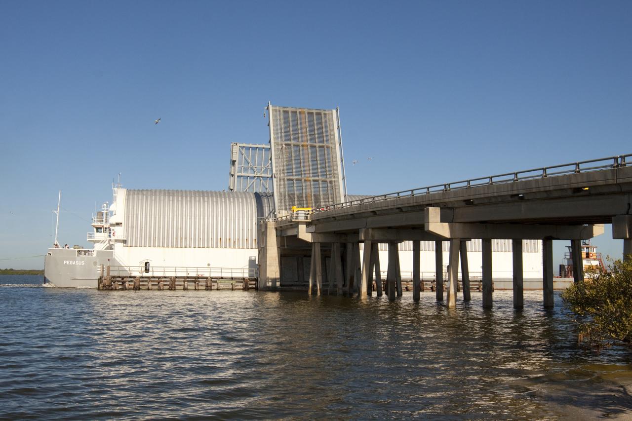CAPE CANAVERAL, Fla. – A tugboat pushes the Pegasus Barge through a drawbridge after leaving NASA's Kennedy Space Center in Florida. The 266-foot-long and 50-foot-wide barge will be towed by NASA's Freedom Star ship to deliver space shuttle main engine (SSME) ground support equipment to Stennis Space Center near Bay St. Louis, Miss. Since being delivered to NASA in 1999, Pegasus sailed 41 times and transported 31 shuttle external fuel tanks from Michoud Assembly Facility near New Orleans to Kennedy. The barge is leaving Kennedy, perhaps for the final time. Both the barge and shuttle equipment will remain in storage until their specific future uses are determined. The SSMEs themselves will be transported to Stennis separately for use with the agency's new heavy-lift rocket, the Space Launch System. The work is part of the Space Shuttle Program’s transition and retirement processing. For more information about Shuttle Transition and Retirement, visit http://www.nasa.gov/mission_pages/transition/home/index.html. Photo credit: NASA/Kim Shiflett