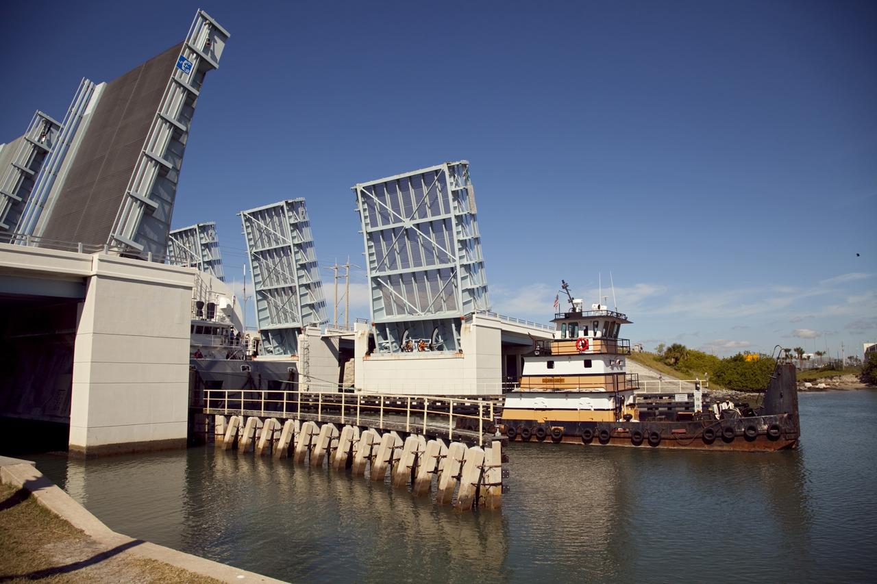 CAPE CANAVERAL, Fla. – A tugboat pulls the Pegasus Barge through a drawbridge after leaving NASA's Kennedy Space Center in Florida. The 266-foot-long and 50-foot-wide barge will be towed by NASA's Freedom Star ship to deliver space shuttle main engine (SSME) ground support equipment to Stennis Space Center near Bay St. Louis, Miss. Since being delivered to NASA in 1999, Pegasus sailed 41 times and transported 31 shuttle external fuel tanks from Michoud Assembly Facility near New Orleans to Kennedy. The barge is leaving Kennedy, perhaps for the final time. Both the barge and shuttle equipment will remain in storage until their specific future uses are determined. The SSMEs themselves will be transported to Stennis separately for use with the agency's new heavy-lift rocket, the Space Launch System. The work is part of the Space Shuttle Program’s transition and retirement processing. For more information about Shuttle Transition and Retirement, visit http://www.nasa.gov/mission_pages/transition/home/index.html. Photo credit: NASA/Frankie Martin