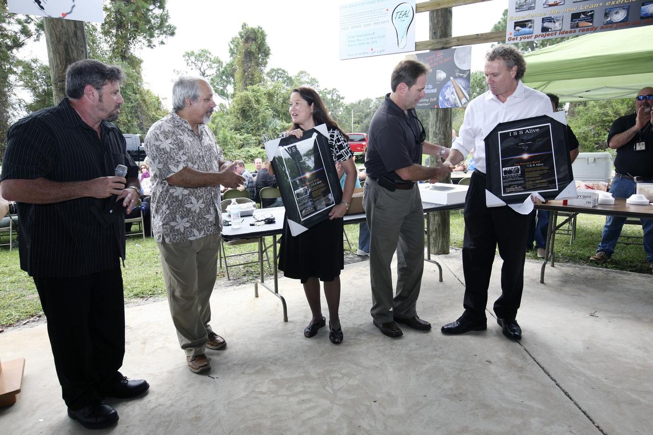 CAPE CANAVERAL, Fla. – International Space Station Ground Processing and Research Project Office Director Josie Burnett, third from left, and Associate Director for Engineering and Technical Operations Russell Romanella, right, are presented plaques and CDs of the song “ISS Alive,” written and recorded by the Panama Band, during the "ISS Is Alive" employee recognition barbecue celebration at Kars Park II at NASA's Kennedy Space Center in Florida. From left are also band members Lew Ingelido, who composed the song, Tom Hadoulias and Norm Tokarz. NASA and The Boeing Co. hosted the celebration to thank the employees based at the Kennedy Space Center who were involved in building the largest, most complex international scientific project in history and the largest venture in space to date.    The station has hosted human life, work and research in space for more than 10 years. Boeing is the prime contractor to NASA for the space station. In addition to designing and building all the major U.S. elements, Boeing also is responsible for ensuring the successful integration of new hardware and software -- including components from international partners -- as well as for providing sustaining engineering work. For more information on the International Space Station, visit http://www.nasa.gov/station.  Photo credit: NASA/Amanda Diller
