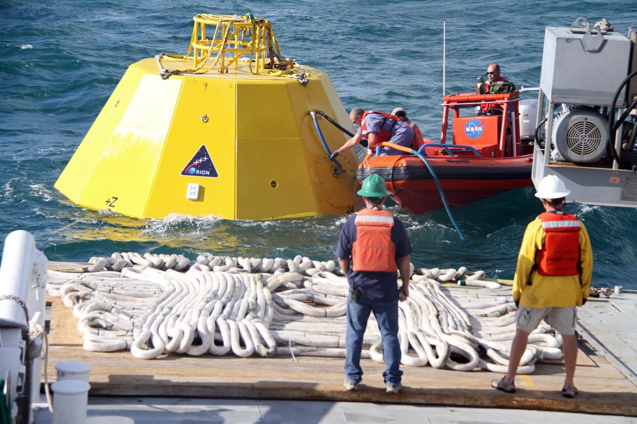 CAPE CANAVERAL, Fla. – From a boat in the Atlantic Ocean, workers secure lines to an Orion flight test capsule during preparations for testing the capsule as their colleagues look on from the deck of NASA's Liberty Star ship. The Crew Module Recovery Attach Fitting Test (CRAFT) on the capsule, which began at-sea operations Nov. 29, is under way. Multiple attach clips are being evaluated against the current recovery cleat configuration by U.S. Air Force pararescue jumpers (PJs) and a U.S. Navy diver. The 21st Century Ground Systems Program will use data collected from the tests to help develop ground operations support equipment that could be used to recover an uncrewed Orion flight test capsule after splashdown. The Orion Multi-Purpose Crew Vehicle is NASA's next-generation spacecraft being developed for deep space missions to asteroids, moons and other interplanetary destinations throughout the solar system. For more information, visit http://www.nasa.gov/orion. Photo credit: NASA/Cory Huston