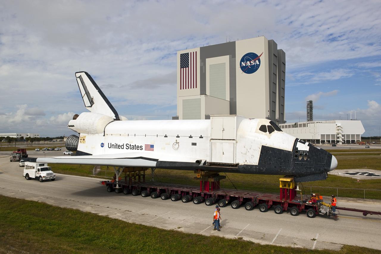 CAPE CANAVERAL, Fla. – Support personnel walk with the high-fidelity space shuttle model which was on display at the NASA Kennedy Space Center Visitor Complex in Florida as it rolls through the parking lot leading to Kennedy's Launch Complex 39 turn basin.  Behind it are the 525-foot-tall Vehicle Assembly Building and the Launch Control Center.     The shuttle was part of a display at the visitor complex that also included an external tank and two solid rocket boosters that were used to show visitors the size of actual space shuttle components. The full-scale shuttle model is being transferred from Kennedy to Space Center Houston, NASA Johnson Space Center's visitor center. The model will stay at the turn basin for a few months until it is ready to be transported to Texas via barge. The move also helps clear the way for the Kennedy Space Center Visitor Complex to begin construction of a new facility next year to display space shuttle Atlantis in 2013.  For more information about Space Center Houston, visit http://www.spacecenter.org.  Photo credit: NASA/Dimitri Gerondidakis
