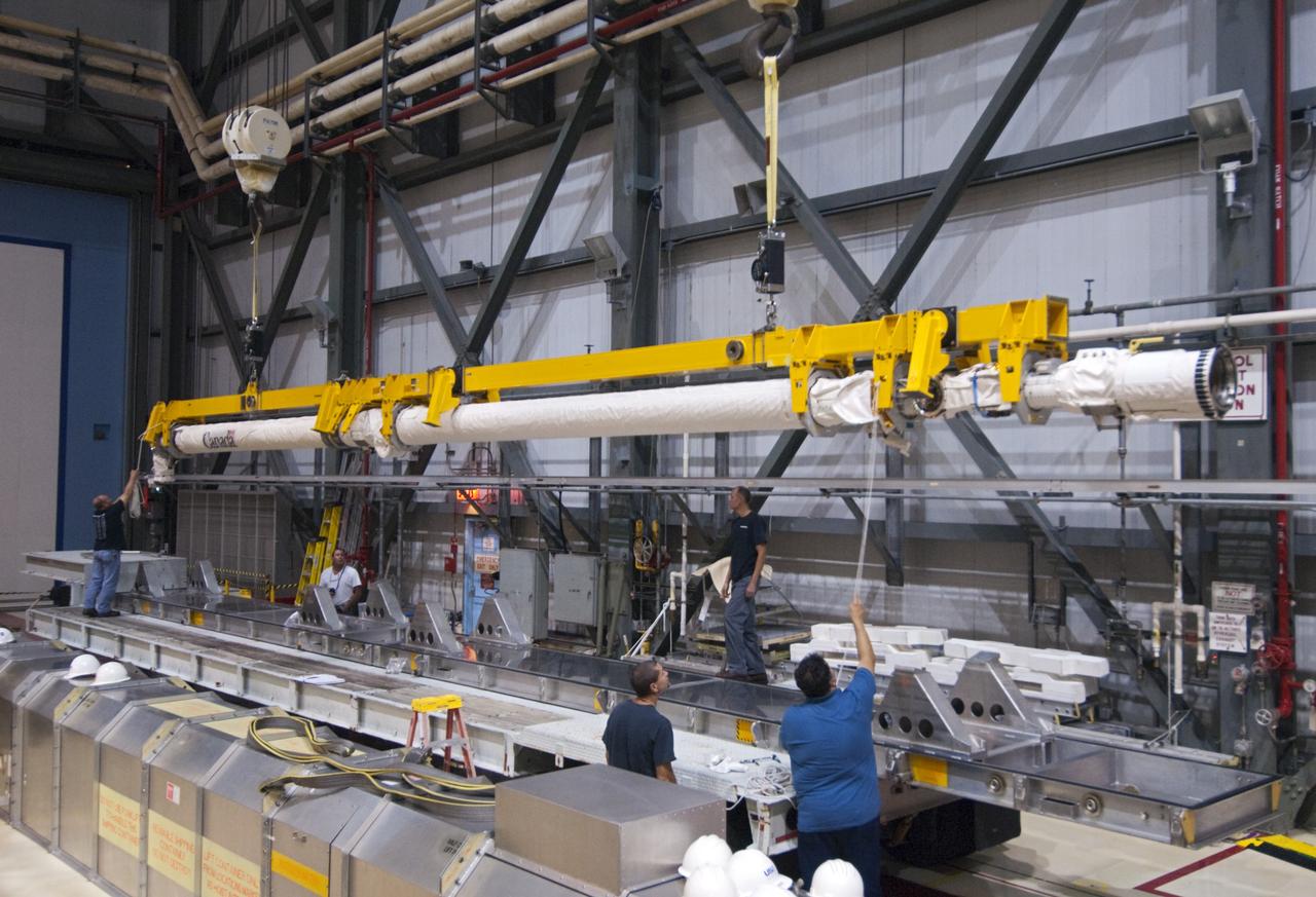 CAPE CANAVERAL, Fla. – Inside Orbiter Processing Facility-2 at NASA’s Kennedy Space Center in Florida, technicians assist as a large crane lowers space shuttle Atlantis’ remote manipulator system (RMS) robotic arm onto a special carrier platform.    The RMS will be transported to NASA’s Johnson Space Center in Houston for possible use on future spaceflights. The work is part of the Space Shuttle Program’s transition and retirement processing of shuttle Atlantis. The shuttle is being prepared for display at the Kennedy Space Center Visitor Complex.  Photo credit: NASA/Jim Grossmann
