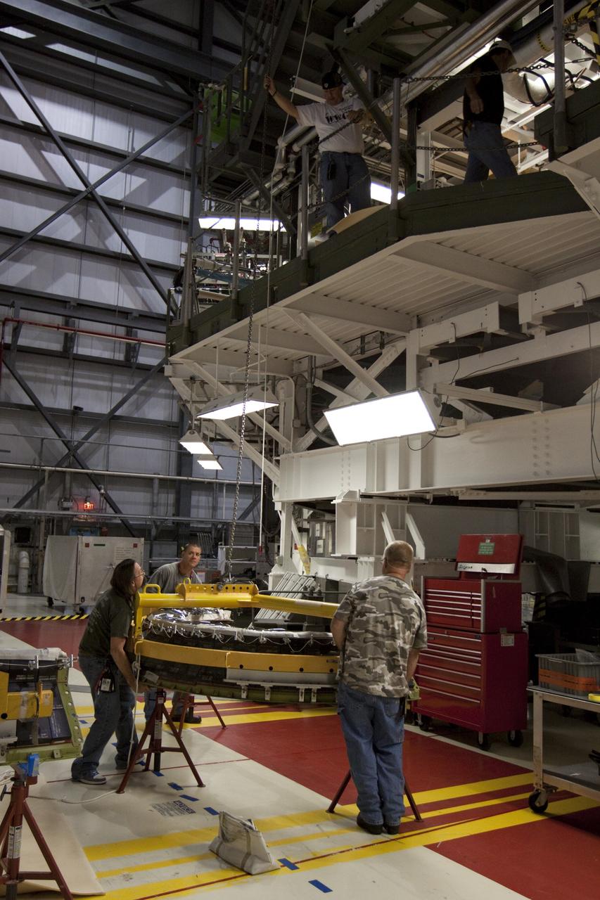 CAPE CANAVERAL, Fla. – Inside Orbiter Processing Facility-1 at NASA’s Kennedy Space Center in Florida, technicians provide assistance as a large crane begins to lift a dome heat shield that will be installed around one of space shuttle Discovery’s three replica shuttle main engines. The dome heat shields are composed of two, semi-circle-shaped sections of thermal protection system tiles that surround the engines. The work is part of the Space Shuttle Program’s transition and retirement processing of shuttle Discovery. Discovery is being prepared for display at the Smithsonian’s National Air and Space Museum, Steven F. Udvar-Hazy Center in Chantilly, Va. For more information, visit http://www.nasa.gov/shuttle. Photo credit: NASA/Kim Shiflett