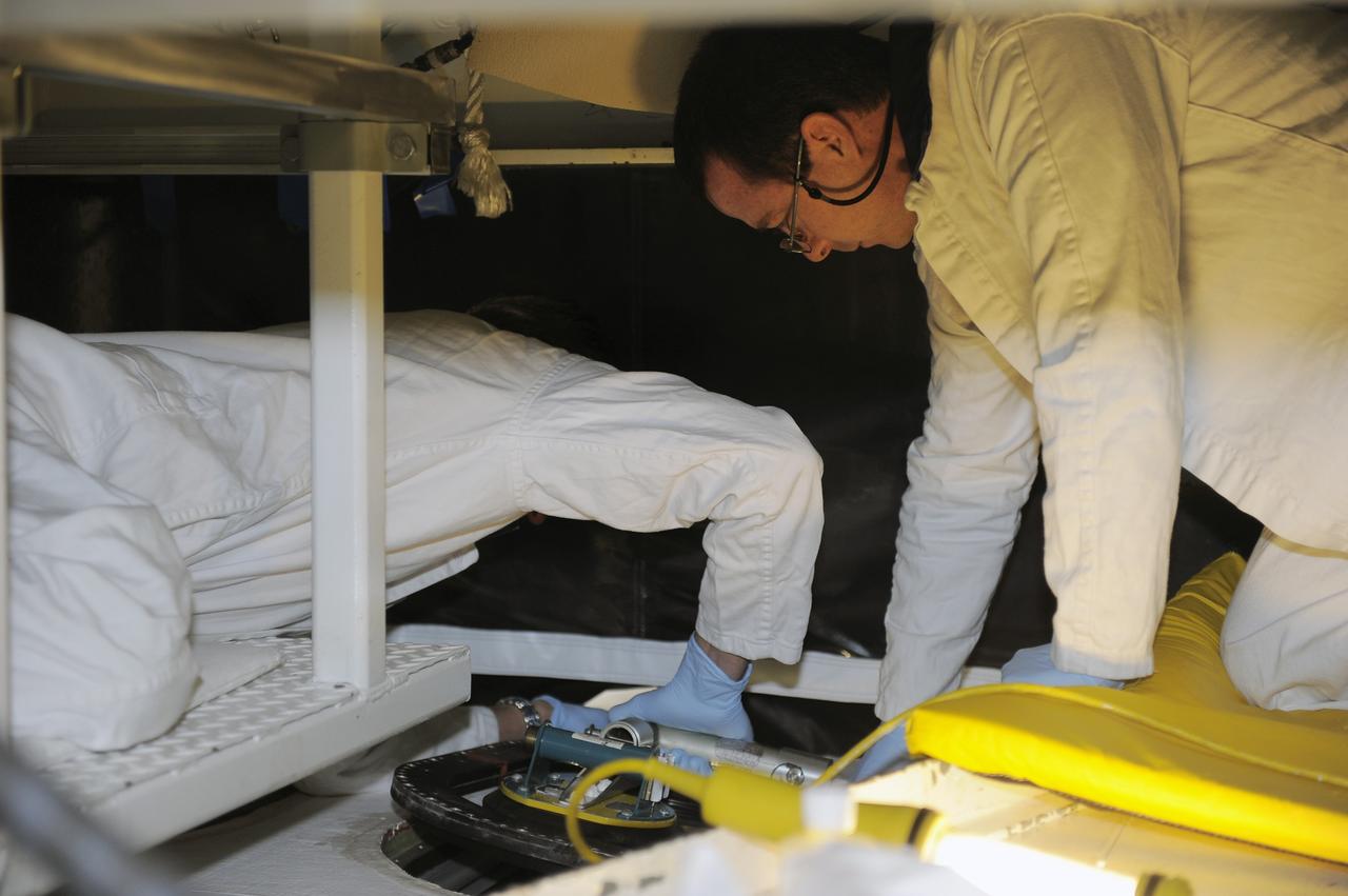 CAPE CANAVERAL, Fla. -- Inside Orbiter Processing Facility-2 at NASA’s Kennedy Space Center in Florida, technicians remove the top emergency escape window from space shuttle Atlantis.     The window is being removed in order to gain access to remove hazardous pyrotechnics from the shuttle. The window will be shipped to Johnson Space Center in Houston for inspections and a replacement outer pane will be installed in its place. The work is part of the Space Shuttle Program’s transition and retirement processing of shuttle Atlantis. The shuttle is being prepared for display at the Kennedy Space Center Visitor Complex in Florida.  Photo credit: NASA/Kim Shiflett
