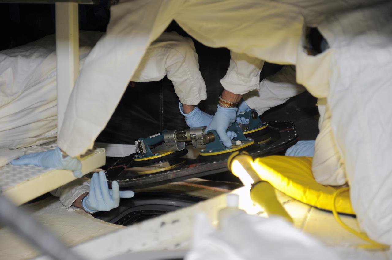 CAPE CANAVERAL, Fla. -- Inside Orbiter Processing Facility-2 at NASA’s Kennedy Space Center in Florida, technicians remove the top emergency escape window from space shuttle Atlantis.     The window is being removed in order to gain access to remove hazardous pyrotechnics from the shuttle. The window will be shipped to Johnson Space Center in Houston for inspections and a replacement outer pane will be installed in its place. The work is part of the Space Shuttle Program’s transition and retirement processing of shuttle Atlantis. The shuttle is being prepared for display at the Kennedy Space Center Visitor Complex in Florida.  Photo credit: NASA/Kim Shiflett