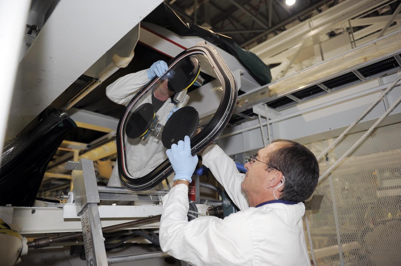 CAPE CANAVERAL, Fla. -- Inside Orbiter Processing Facility-2 at NASA’s Kennedy Space Center in Florida, technicians remove the top emergency escape window from space shuttle Atlantis.     The window is being removed in order to gain access to remove hazardous pyrotechnics from the shuttle. The window will be shipped to Johnson Space Center in Houston for inspections and a replacement outer pane will be installed in its place. The work is part of the Space Shuttle Program’s transition and retirement processing of shuttle Atlantis. The shuttle is being prepared for display at the Kennedy Space Center Visitor Complex in Florida.  Photo credit: NASA/Kim Shiflett