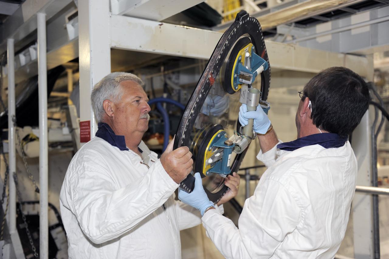 CAPE CANAVERAL, Fla. -- Inside Orbiter Processing Facility-2 at NASA’s Kennedy Space Center in Florida, technicians inspect the top emergency escape window that was removed from space shuttle Atlantis.    The window is being removed in order to gain access to remove hazardous pyrotechnics from the shuttle. The window will be shipped to Johnson Space Center in Houston for inspections and a replacement outer pane will be installed in its place. The work is part of the Space Shuttle Program’s transition and retirement processing of shuttle Atlantis. The shuttle is being prepared for display at the Kennedy Space Center Visitor Complex in Florida.  Photo credit: NASA/Kim Shiflett