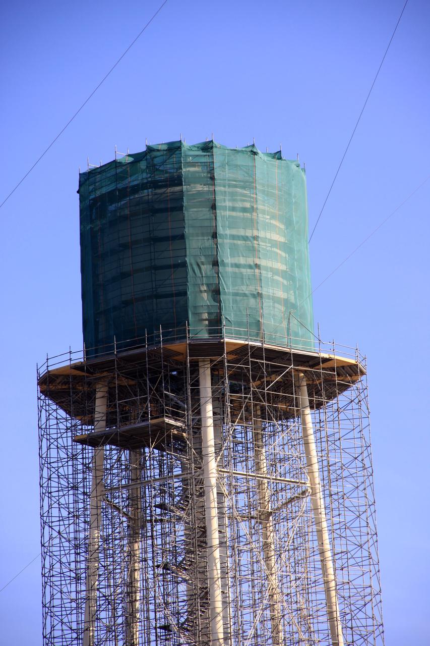 CAPE CANAVERAL, Fla. - At NASA’s Kennedy Space Center in Florida, preparations are underway to sandblast and paint the 290-foot-high water tower at Launch Pad 39B. Scaffolding surrounds the tower and a special covering has been placed around the tank.    The water towers at Launch Complex 39, which includes pad A and B, were part of the sound suppression system used during space shuttle launches. Water stored in the 300,000-gallon tank would be released just prior to main engine ignition and flow by gravity to special mobile launcher platform (MLP) outlets. Nine seconds after shuttle liftoff, the peak flow rate was 900,000 gallons per minute and helped to protect the orbiter and payloads from being damaged by acoustical energy reflected from the MLP during liftoff. Photo Credit: NASA/Jim Grossmann