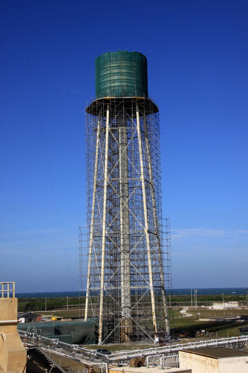 CAPE CANAVERAL, Fla. - At NASA’s Kennedy Space Center in Florida, preparations are underway to sandblast and paint the 290-foot-high water tower at Launch Pad 39B. Scaffolding surrounds the tower and a special covering has been placed around the tank.    The water towers at Launch Complex 39, which includes pad A and B, were part of the sound suppression system used during space shuttle launches. Water stored in the 300,000-gallon tank would be released just prior to main engine ignition and flow by gravity to special mobile launcher platform (MLP) outlets. Nine seconds after shuttle liftoff, the peak flow rate was 900,000 gallons per minute and helped to protect the orbiter and payloads from being damaged by acoustical energy reflected from the MLP during liftoff. Photo Credit: NASA/Jim Grossmann