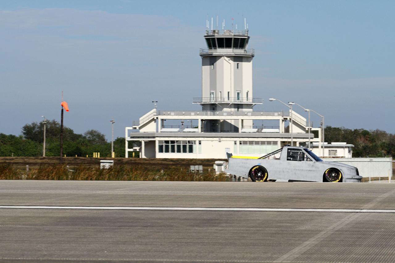 CAPE CANAVERAL, Fla. - At NASA’s Kennedy Space Center in Florida, NASCAR racer Jason Leffler with Kyle Busch Motorsports (KBM) drives his instrument-laden vehicle down the three-mile-long Shuttle Landing Facility runway. In the background, at midfield is the Control Tower. The operation is part of KBMs’ program to test aerodynamic and real-world capabilities on one of the flattest surfaces in the world.    Racing teams have been using the runway for testing since 2008. KBM signed a Space Act Agreement with NASA to use the facility’s runway. Photo Credit: NASA/Kim Shiflett