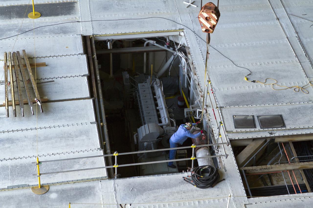 CAPE CANAVERAL, Fla. –Inside the Vehicle Assembly Building at NASA’s Kennedy Space Center in Florida, a worker helps guide a crane as it is lowered toward crawler-transporter 2 CT-2) so that the Apollo era diesel engine can be removed. New engines will be installed later this month. Work is in progress in high bay 2 to upgrade CT-2 so that it can carry NASA’s Space Launch System heavy-lift rocket, which is under design, and new Orion spacecraft to the launch pad. The crawler-transporters were used to carry the mobile launcher platform and space shuttle to Launch Complex 39 for space shuttle launches for 30 years. Photo credit: NASA/Kim Shiflett