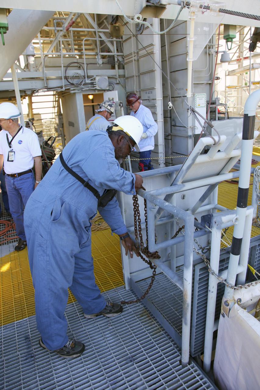 CAPE CANAVERAL, Fla. – At Launch Pad 39A at NASA’s Kennedy Space Center in Florida, technicians prepare for the final release of the seven slidewire baskets from the 195-foot level. After the baskets reach the ground they will be removed and put in storage.    The system of seven slidewire baskets at launch pads A and B provided an escape route for personnel inside the orbiter or on the orbiter access arm. The baskets are suspended from slidewires that extend from the pad’s Fixed Service Structure to a landing zone 1,200 feet to the west. Each basket could hold up to three people. A braking system catch net and drag chain slowed and then halted the baskets sliding down the wire approximately 55 miles per hour in about half a minute. Photo credit: NASA/Frankie Martin