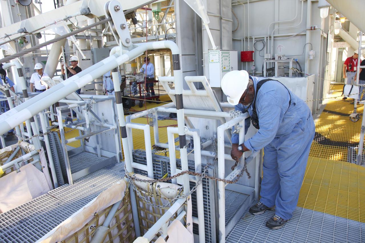 CAPE CANAVERAL, Fla. – At Launch Pad 39A at NASA’s Kennedy Space Center in Florida, technicians prepare for the final release of the seven slidewire baskets from the 195-foot level. After the baskets reach the ground they will be removed and put in storage.    The system of seven slidewire baskets at launch pads A and B provided an escape route for personnel inside the orbiter or on the orbiter access arm. The baskets are suspended from slidewires that extend from the pad’s Fixed Service Structure to a landing zone 1,200 feet to the west. Each basket could hold up to three people. A braking system catch net and drag chain slowed and then halted the baskets sliding down the wire approximately 55 miles per hour in about half a minute. Photo credit: NASA/Frankie Martin