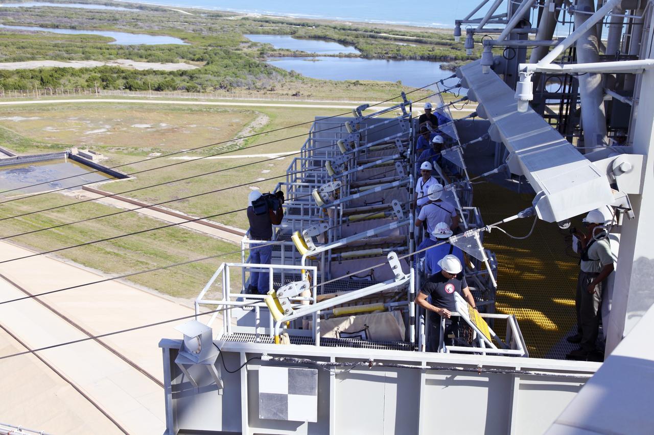 CAPE CANAVERAL, Fla. – At Launch Pad 39A at NASA’s Kennedy Space Center in Florida, technicians prepare for the final release of the seven slidewire baskets from the 195-foot level. After the baskets reach the ground they will be removed and put in storage.    The system of seven slidewire baskets at launch pads A and B provided an escape route for personnel inside the orbiter or on the orbiter access arm. The baskets are suspended from slidewires that extend from the pad’s Fixed Service Structure to a landing zone 1,200 feet to the west. Each basket could hold up to three people. A braking system catch net and drag chain slowed and then halted the baskets sliding down the wire approximately 55 miles per hour in about half a minute. Photo credit: NASA/Frankie Martin