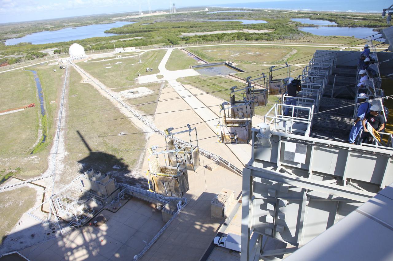 CAPE CANAVERAL, Fla. – At Launch Pad 39A at NASA’s Kennedy Space Center in Florida, technicians have released the seven slidewire baskets from the 195-foot level for the final time. After the baskets reach the ground they will be removed and put in storage.    The system of seven slidewire baskets at launch pads A and B provided an escape route for personnel inside the orbiter or on the orbiter access arm. The baskets are suspended from slidewires that extend from the pad’s Fixed Service Structure to a landing zone 1,200 feet to the west. Each basket could hold up to three people. A braking system catch net and drag chain slowed and then halted the baskets sliding down the wire approximately 55 miles per hour in about half a minute. Photo credit: NASA/Frankie Martin