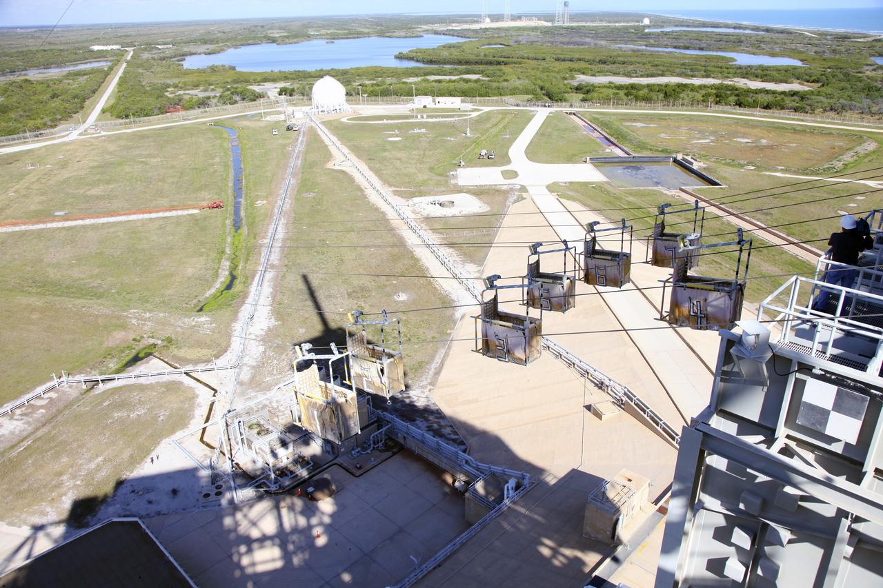 CAPE CANAVERAL, Fla. – At Launch Pad 39A at NASA’s Kennedy Space Center in Florida, technicians have released the seven slidewire baskets from the 195-foot level for the final time. After the baskets reach the ground they will be removed and put in storage.    The system of seven slidewire baskets at launch pads A and B provided an escape route for personnel inside the orbiter or on the orbiter access arm. The baskets are suspended from slidewires that extend from the pad’s Fixed Service Structure to a landing zone 1,200 feet to the west. Each basket could hold up to three people. A braking system catch net and drag chain slowed and then halted the baskets sliding down the wire approximately 55 miles per hour in about half a minute. Photo credit: NASA/Frankie Martin
