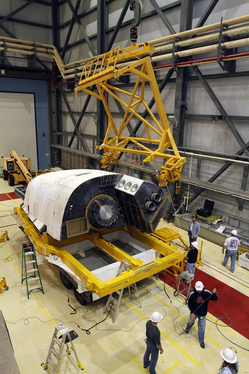 CAPE CANAVERAL, Fla. – In Orbiter Processing Facility-2 at NASA’s Kennedy Space Center in Florida, United Space Alliance technicians monitor the progress as a large crane is lowered toward the right orbital maneuvering system OMS pod that will be installed on space shuttle Endeavour. The OMS pod underwent complete deservicing and cleaning at White Sands Space Harbor in New Mexico, part of the transition and retirement processing of each shuttle. Endeavour is being prepared for public display at the California Science Center in Los Angeles. Over the course of its 19-year career, Endeavour spent 299 days in space during 25 missions. For more information, visit http://www.nasa.gov/shuttle. Photo credit: NASA/Kim Shiflett