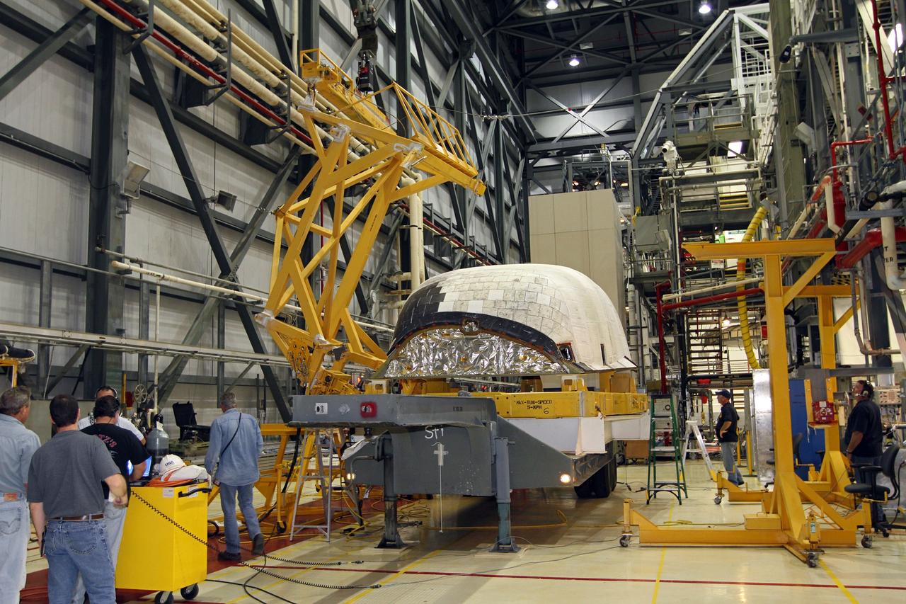 CAPE CANAVERAL, Fla. – In Orbiter Processing Facility-2 at NASA’s Kennedy Space Center in Florida, United Space Alliance technicians monitor the progress as a large crane is lowered toward the right orbital maneuvering system OMS pod that will be installed on space shuttle Endeavour. The OMS pod underwent complete deservicing and cleaning at White Sands Space Harbor in New Mexico, part of the transition and retirement processing of each shuttle. Endeavour is being prepared for public display at the California Science Center in Los Angeles. Over the course of its 19-year career, Endeavour spent 299 days in space during 25 missions. For more information, visit http://www.nasa.gov/shuttle. Photo credit: NASA/Kim Shiflett
