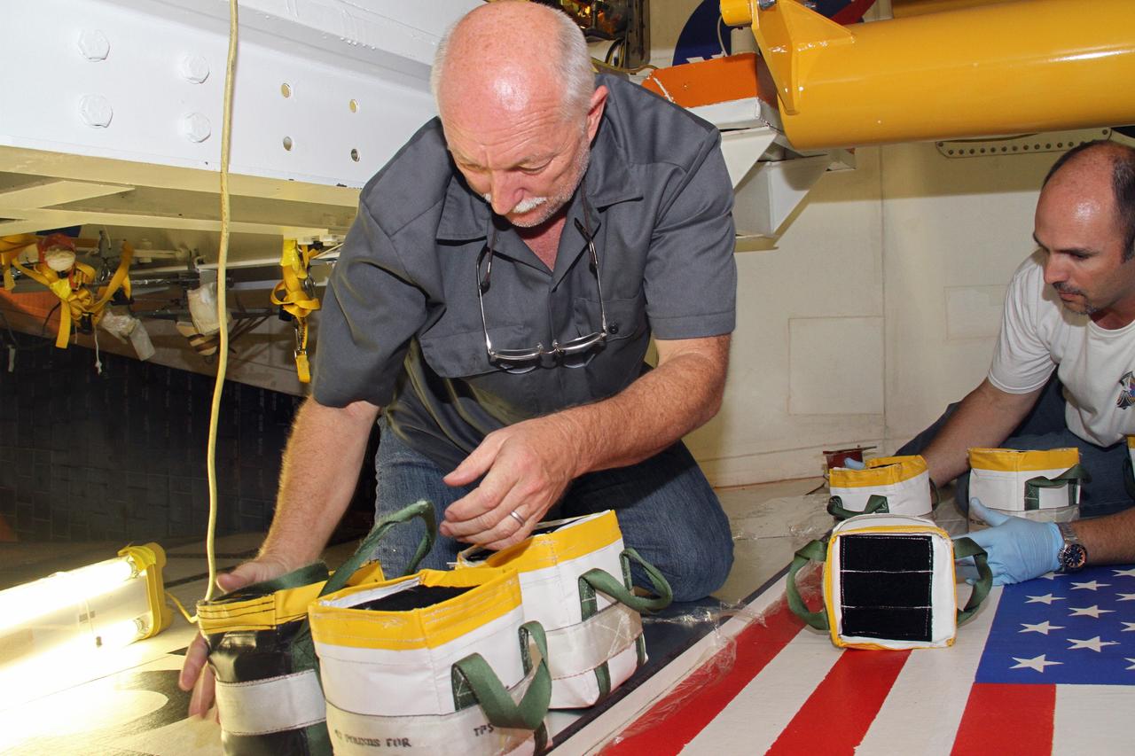 CAPE CANAVERAL, Fla. – Mike Williams, left, a thermal protection system technician, and Jeremy Schwarz, right, quality assurance technician, both with United Space Alliance, set weights atop a newly installed section of tile on the right wing of space shuttle Endeavour at NASA's Kennedy Space Center in Florida. The weights will hold the section in place while the adhesive hardens beneath.    Ongoing transition and retirement activities are preparing the spacecraft for public display at the California Science Center in Los Angeles. Endeavour flew 25 missions during its 19-year career. Photo credit: NASA/Cory Huston