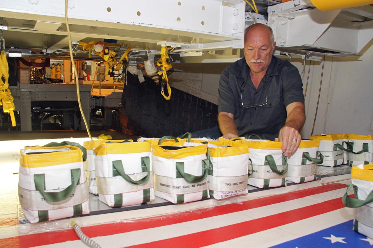 CAPE CANAVERAL, Fla. – Mike Williams, a thermal protection system technician with United Space Alliance, arranges weights atop a freshly installed section of tile on the right wing of space shuttle Endeavour at NASA's Kennedy Space Center in Florida. The weights will hold the section in place while the adhesive hardens beneath.    Ongoing transition and retirement activities are preparing the spacecraft for public display at the California Science Center in Los Angeles. Endeavour flew 25 missions during its 19-year career. Photo credit: NASA/Cory Huston