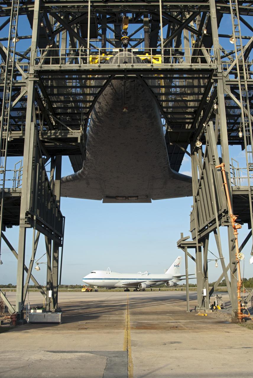 CAPE CANAVERAL, Fla. – At the Shuttle Landing Facility at NASA’s Kennedy Space Center in Florida, space shuttle Discovery is suspended 60 feet off the ground inside the mate-demate device in preparation for the arrival of the Shuttle Carrier Aircraft, in the background.  The device, known as the MDD, is a large gantry-like steel structure used to hoist a shuttle off the ground and position it onto the back of the aircraft, or SCA. The SCA is a Boeing 747 jet, originally manufactured for commercial use, which was modified by NASA to transport the shuttles between destinations on Earth. The SCA designated NASA 905 is assigned to the remaining ferry missions, delivering the shuttles to their permanent public display sites.  NASA 905 is scheduled to ferry Discovery to the Washington Dulles International Airport in Virginia on April 17, after which the shuttle will be placed on display in the Smithsonian's National Air and Space Museum Steven F. Udvar-Hazy Center. For more information on the SCA, visit http://www.nasa.gov/centers/dryden/news/FactSheets/FS-013-DFRC.html. For more information on shuttle transition and retirement activities, visit http://www.nasa.gov/transition.  Photo credit: NASA/Tim Jacobs